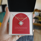 Hand holding open gift box with 14K white gold finish Christian Christmas Love Knot necklace and Luke 2:11 modern message card