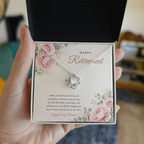 Hand holding open gift box with 14K white gold finish Retirement Love Knot necklace for Her and "Happy Retirement" message card