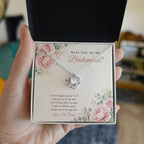 Hand holding open gift box with 14K white gold finish Bridesmaid Proposal Love Knot necklace for Bridesmaid and "Will You Be My Bridesmaid?" message card