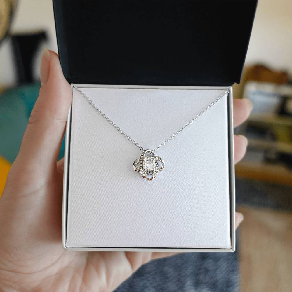 Hand holding open gift box with silver finish Christian Christmas Love Knot necklace and John 3:16 message card