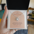 Hand holding open gift box with 14K white gold finish Christian Love Knot necklace for Anniversary and 1 Corinthians 13:7 modern message card