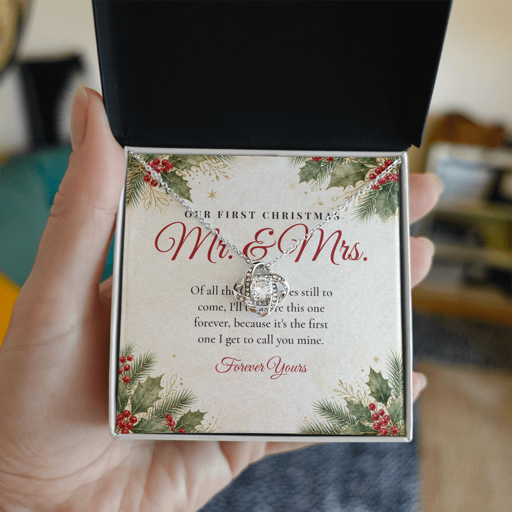 Hand holding gift box with silver Love Knot necklace for wife and Our First Christmas Mr. & Mrs. message card