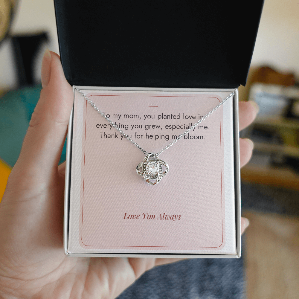 Hand holding gift box with white gold Love Knot necklace for Mom and Helping Me Bloom message card