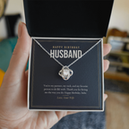 Hand holding open gift box with 14K white gold finish Birthday Love Knot necklace for Husband and "Happy Birthday Husband" message card