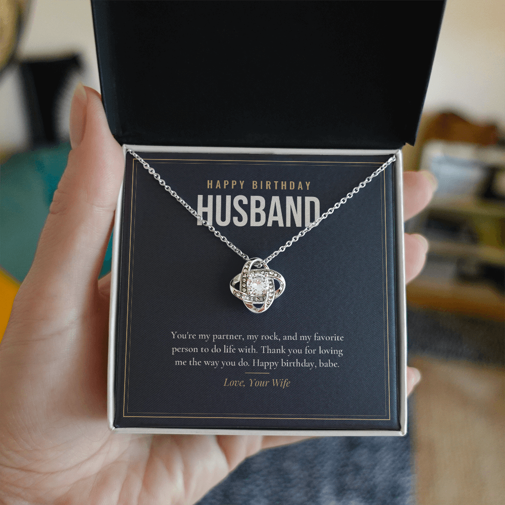 Hand holding open gift box with 14K white gold finish Birthday Love Knot necklace for Husband and "Happy Birthday Husband" message card