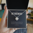 Hand holding open gift box with 14K white gold finish Retirement Love Knot necklace for Him and "Happy Retirement" message card