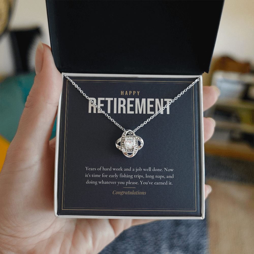 Hand holding open gift box with 14K white gold finish Retirement Love Knot necklace for Him and "Happy Retirement" message card