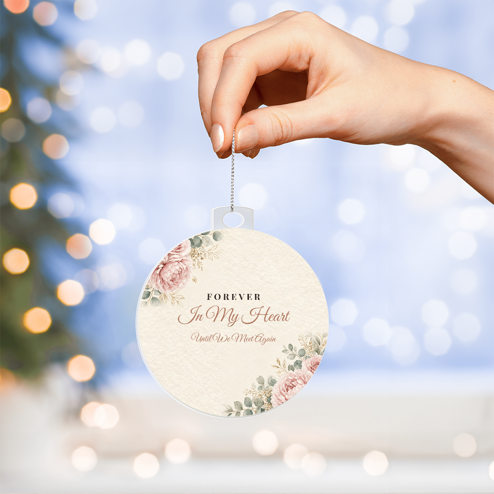 Hand hanging acrylic bulb ornament with Forever In My Heart design in front of Christmas tree lights