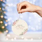 Hand hanging acrylic bulb ornament with Forever In My Heart design in front of Christmas tree lights