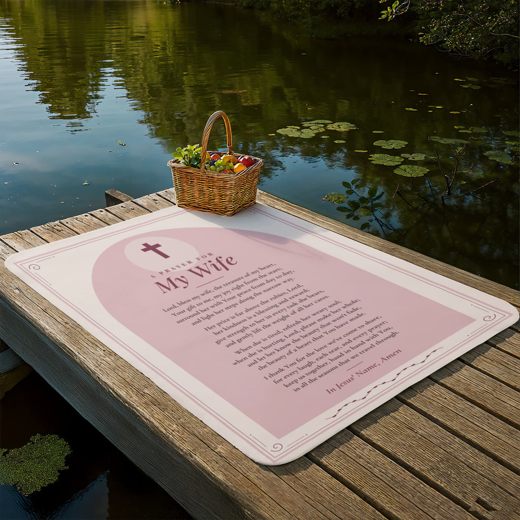 Blush pink prayer blanket for wife laid out on a lakeside dock with picnic basket