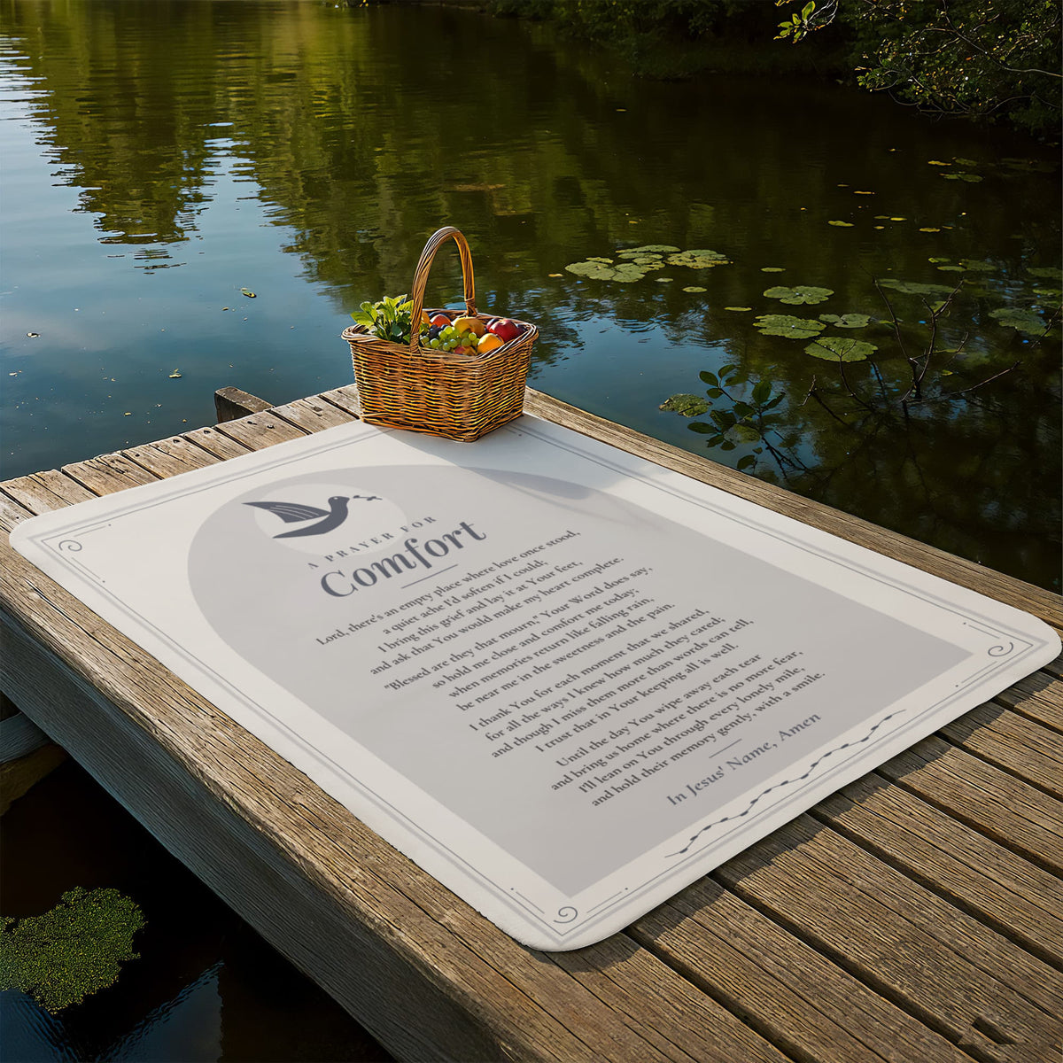 Gray comfort prayer blanket laid out on a lakeside dock with picnic basket