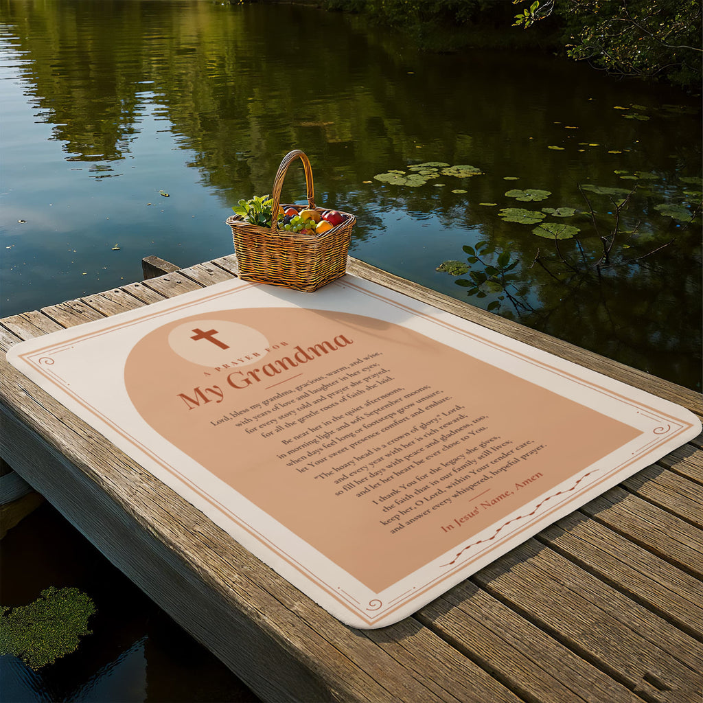 Peach prayer blanket for grandma laid out on a lakeside dock with picnic basket